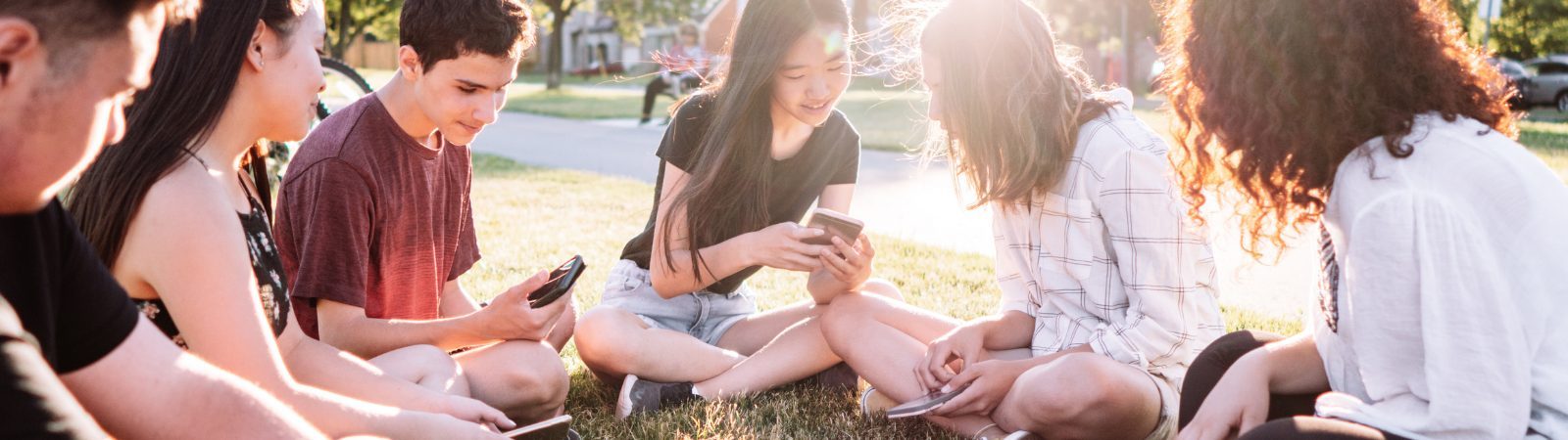 Group of young teenagers sitting outside in a circle showing each other images on their phones