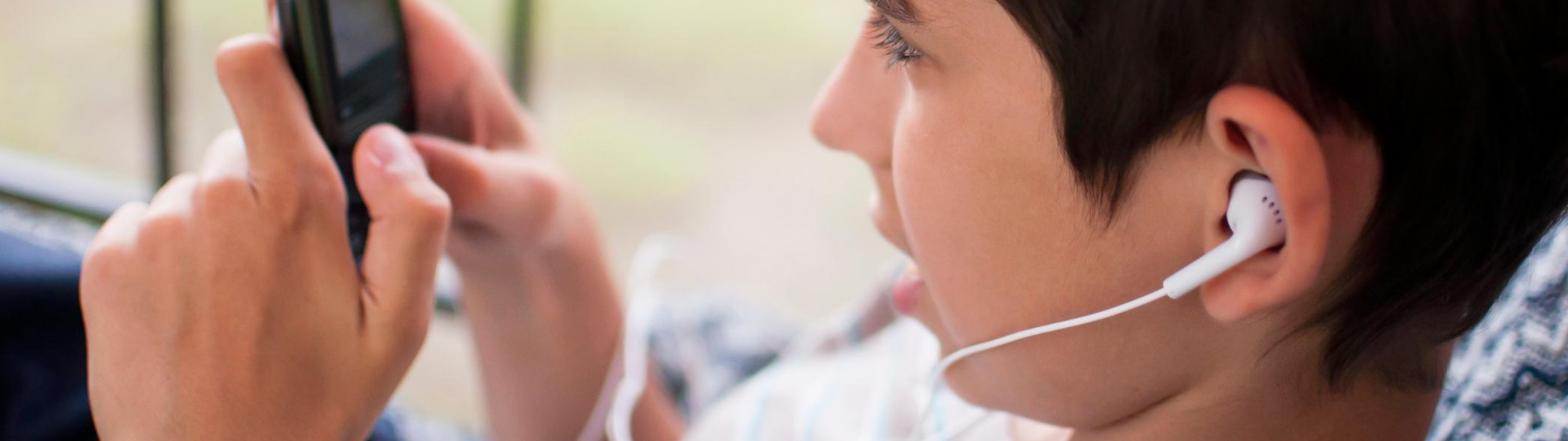 Teenage boy looking at phone and llistening to music with earbuds in his ears.