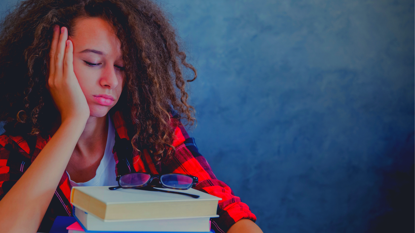 Teenager sleeping over a pile of books