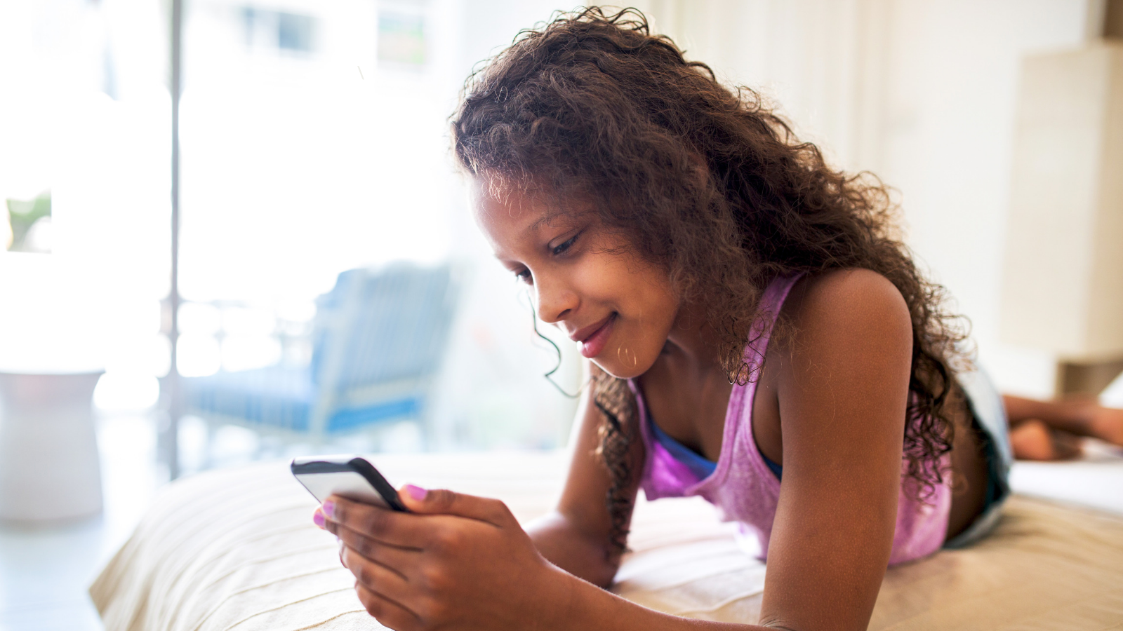 Teenager laying on bed looking at cell phone with parental controls on it.