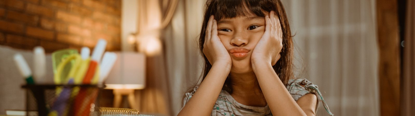 Frustrated child sitting at table with her head in her hands 