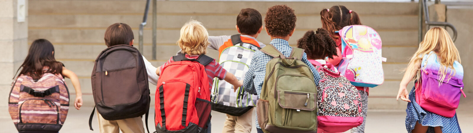 Group of kids running towards school with their backpacks on