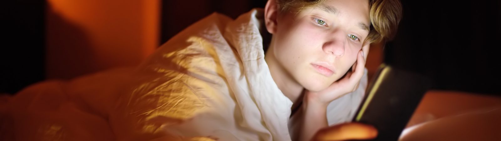 Teen boy laying on bed looking at internet on phone