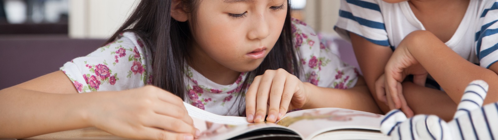 Child laying on bed reading a book to another child