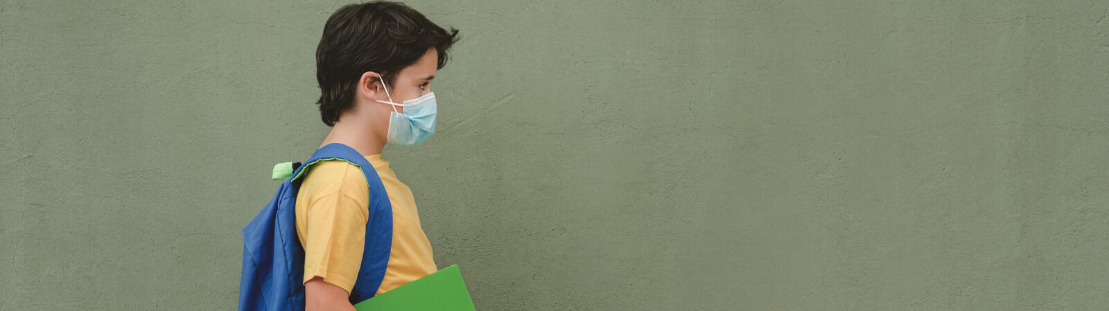 Student wearing a yellow t-shirt and a blue backpack going to school with a mask on during COVID-19 pandemic