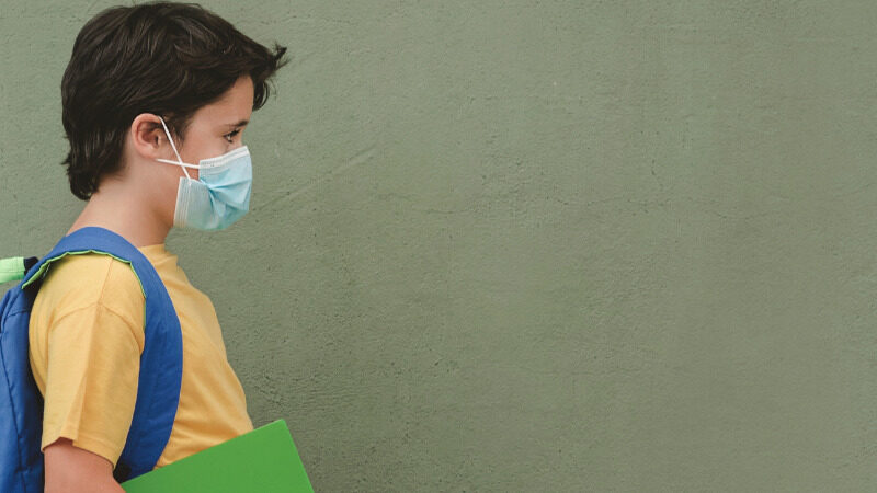 Student wearing a yellow t-shirt and a blue backpack going to school with a mask on during COVID-19 pandemic