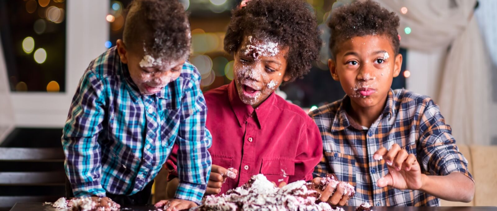 Three kids eating cake at the dining room table with crumbs all over their faces