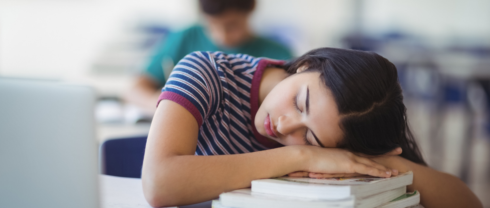 Teenager sleeping at desk on a pile of books at school